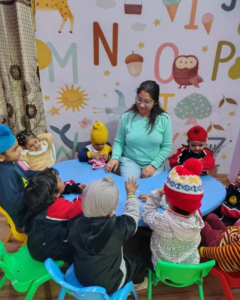 Poonam Sharma, our founder, at the round table with a small group of children beneath the alphabet mural