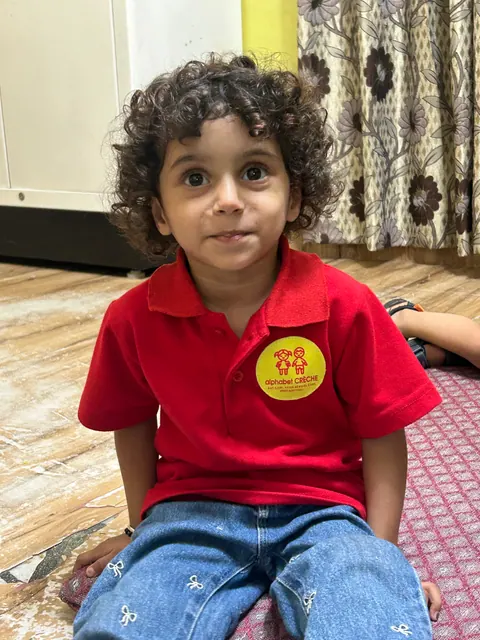 A curly-haired boy in the red alphabet CRÈCHE polo with the logo