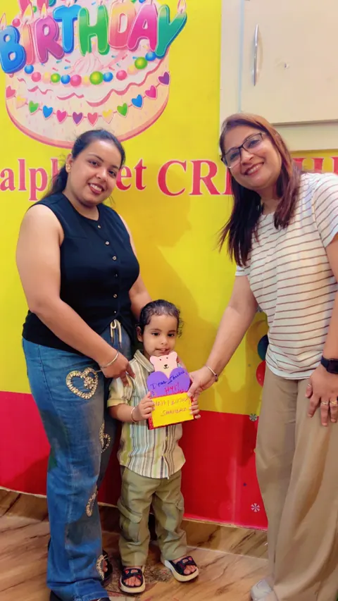 A birthday child with two teachers in front of the alphabet CRÈCHE birthday wall