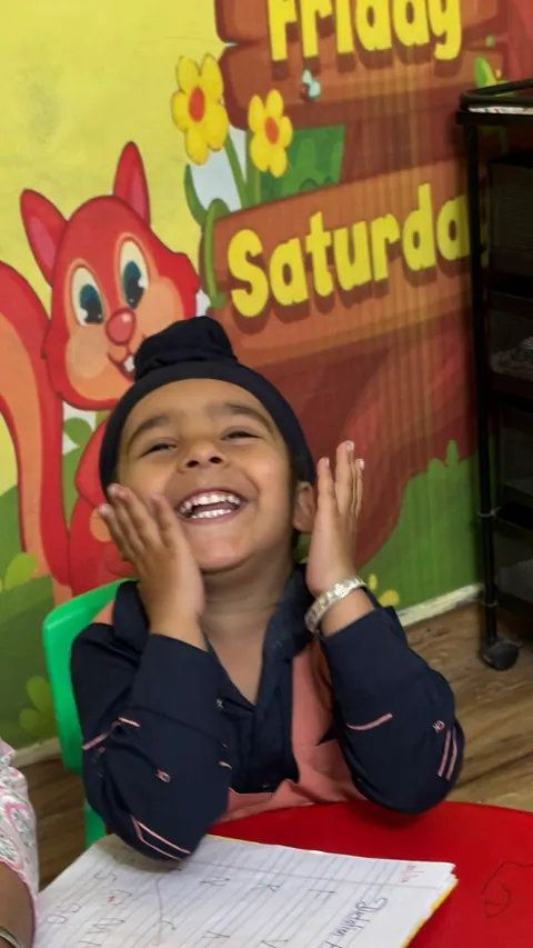 A boy laughing with his hands on his cheeks in front of a colourful classroom mural