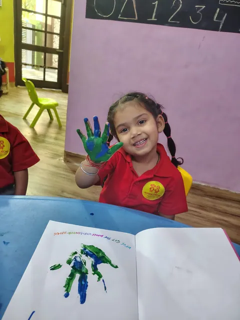 A little girl in the red alphabet CRÈCHE uniform proudly showing her green and blue painted hand, at the centre in Anand Nagar B, Patiala