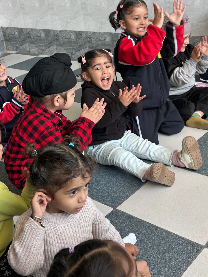 Children sitting on the floor of the playing area, clapping and singing