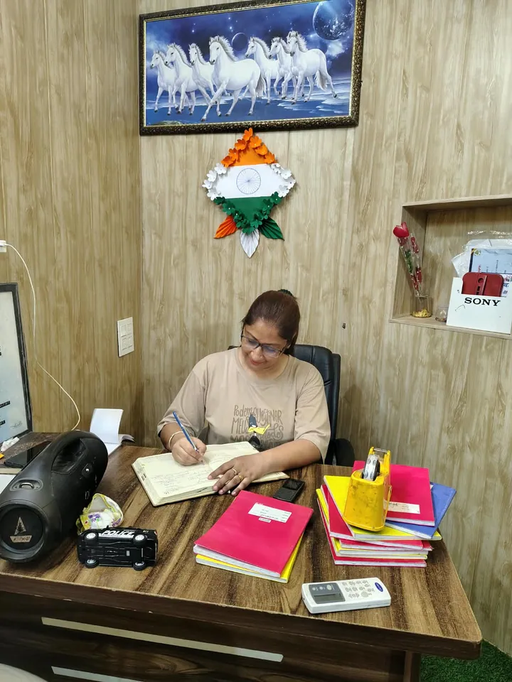 Poonam ma'am writing in a register at her desk in the office