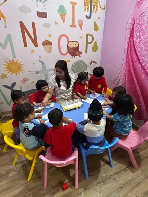 A teacher with a small group of children at a round table, beneath the alphabet wall mural