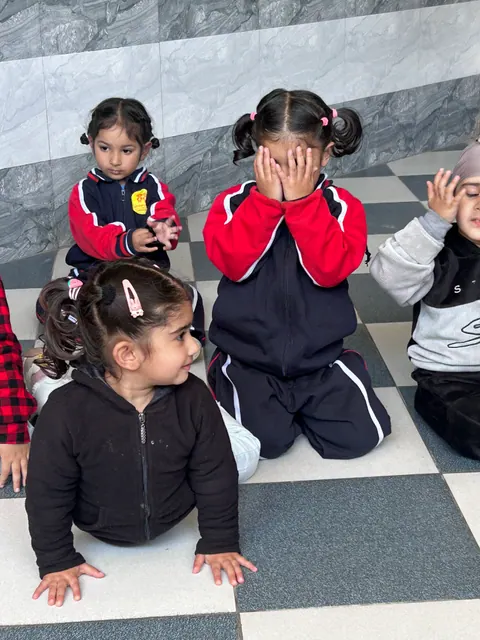 Toddlers playing peekaboo on the floor, one hiding her face in her hands