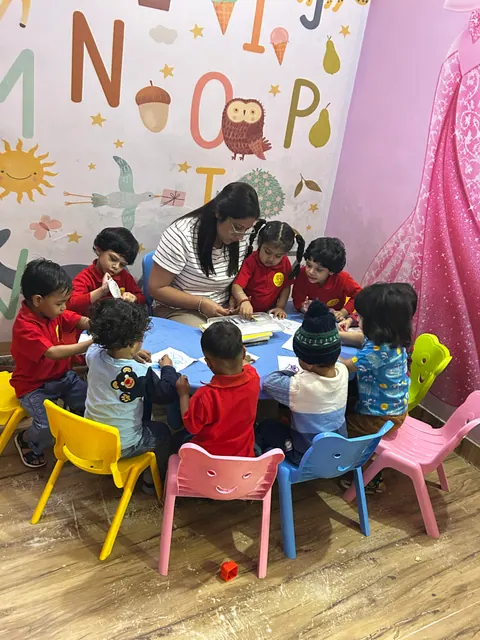 A teacher with a small group of children in uniform at a round table, beneath the alphabet wall