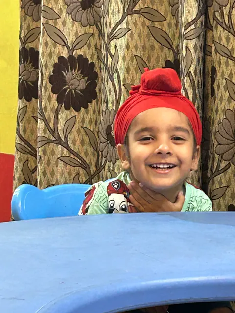 A little boy in a red patka smiling at the classroom table