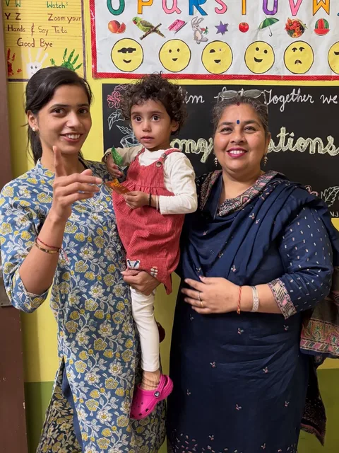 Two members of staff with a toddler in front of the alphabet chart