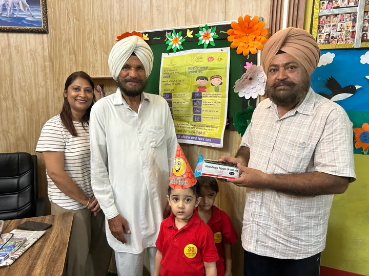 In the office, the birthday child in a party hat is handed a present, with Poonam ma’am beside them