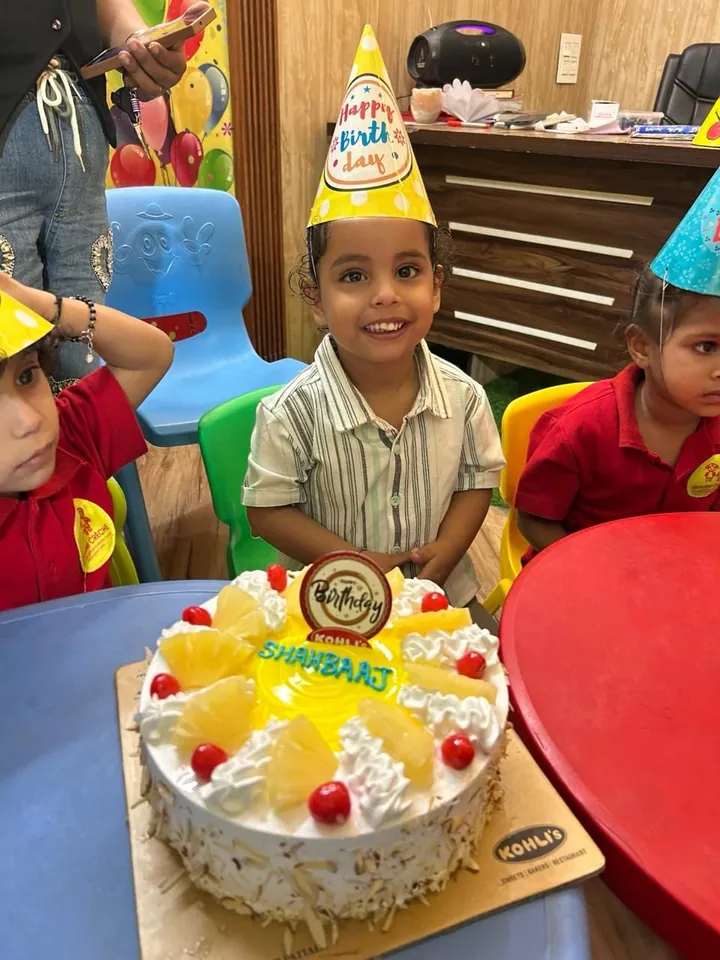 The birthday boy in a party hat smiles behind his pineapple cake