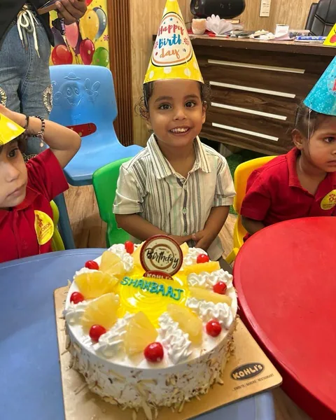 The birthday boy in a party hat smiles behind his pineapple cake