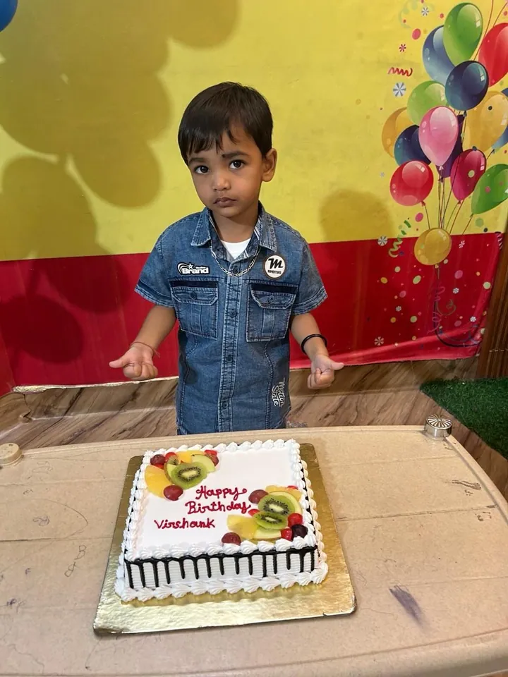 The birthday boy stands by his cake in front of the balloon wall