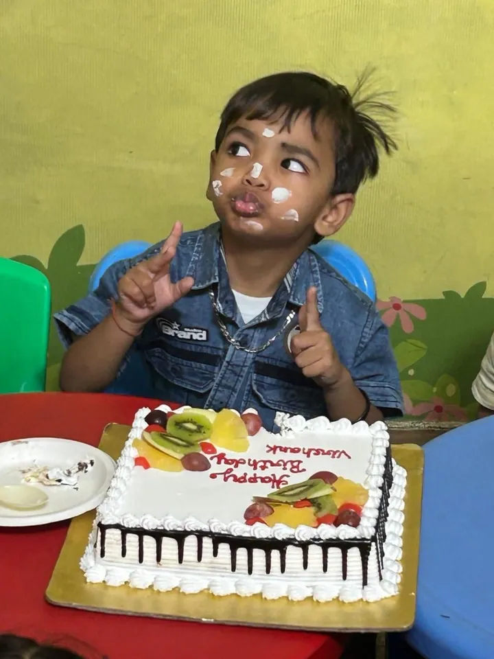 The birthday boy with cream on his cheeks points at the camera