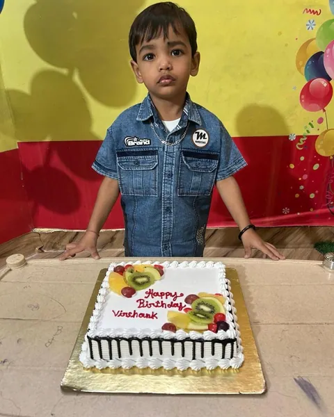 A little boy in a denim shirt stands behind his fruit-topped birthday cake