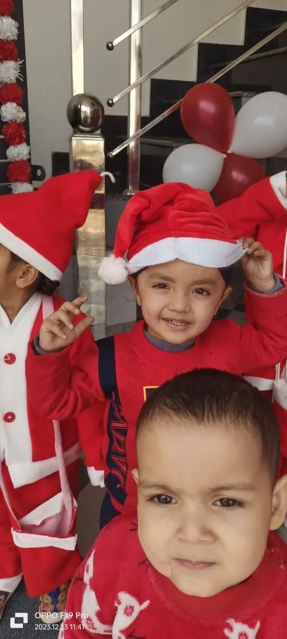 Two small children in Santa hats under the balloons, one grinning at the camera
