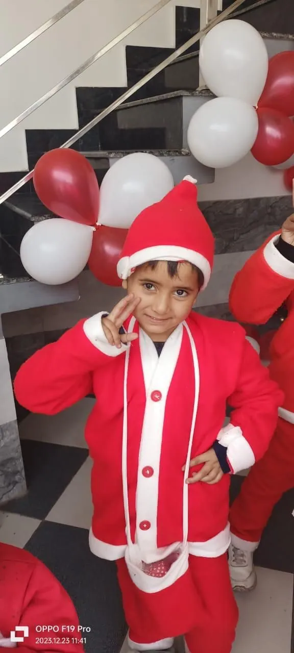A boy in a full Santa suit poses with one hand on his hip at the foot of the stairs
