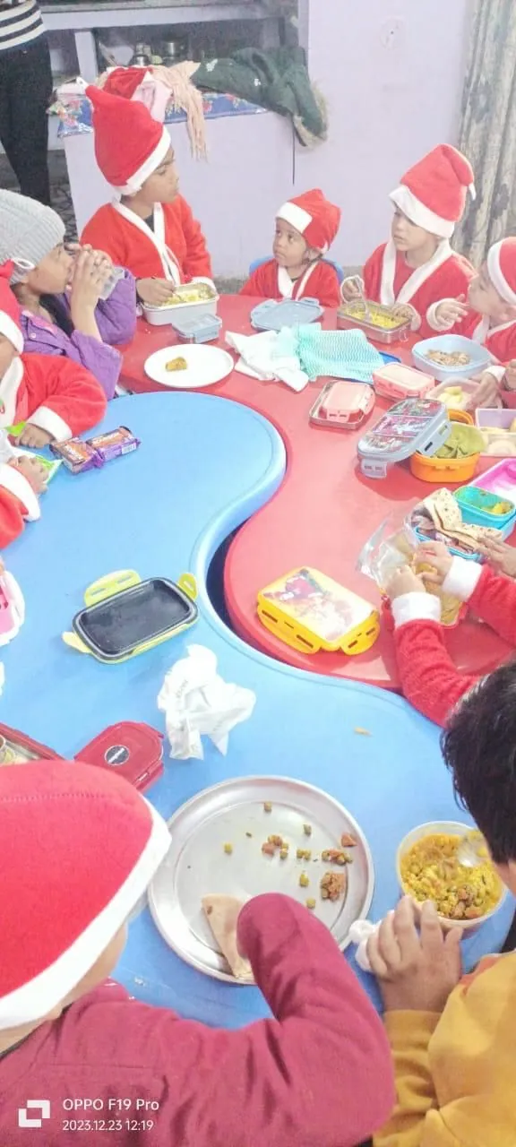 Children in Santa hats sit round the blue table with their own tiffin boxes