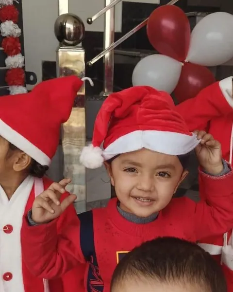Two small children in Santa hats under the balloons, one grinning at the camera