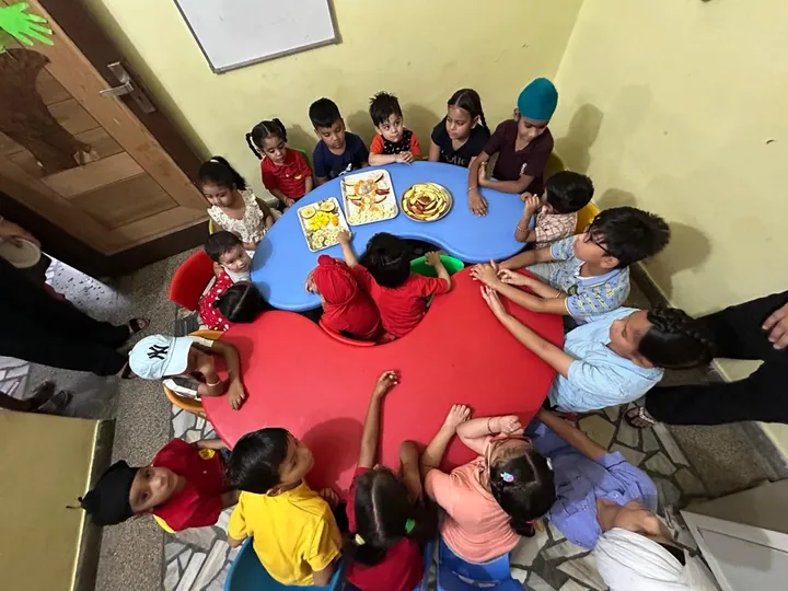 Children in the red uniform gather round the red and blue tables