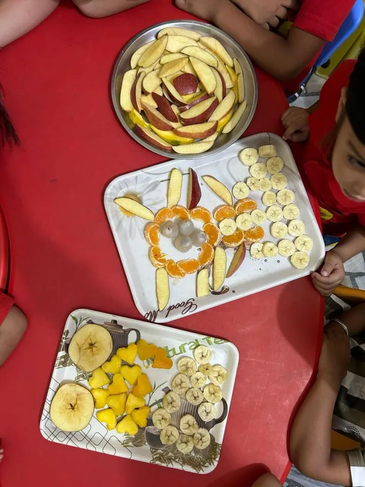 Plates of apple, orange and banana slices arranged into flower shapes on the red table