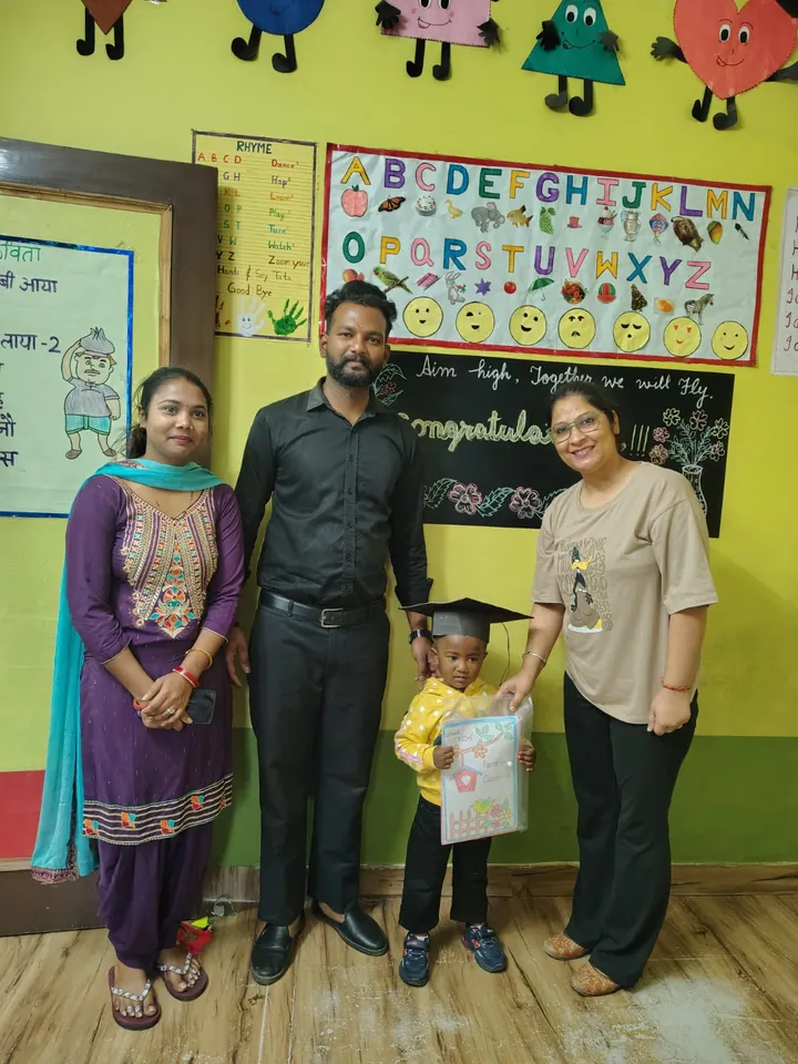 Poonam ma'am hands a certificate to a small graduate in a cap, with the family beside them