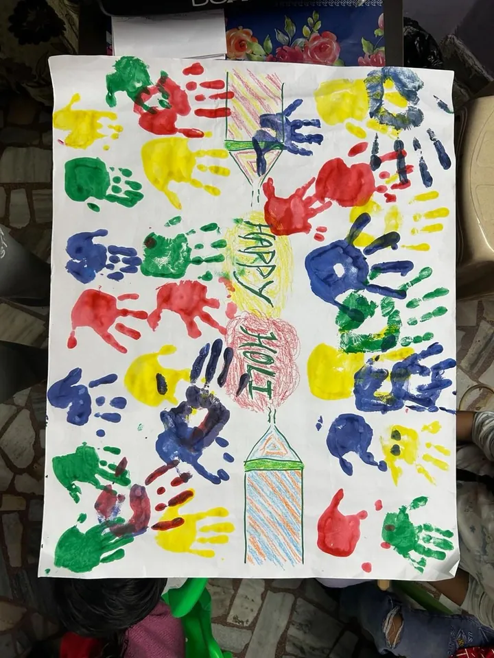 A Happy Holi chart covered in bright handprints in every colour