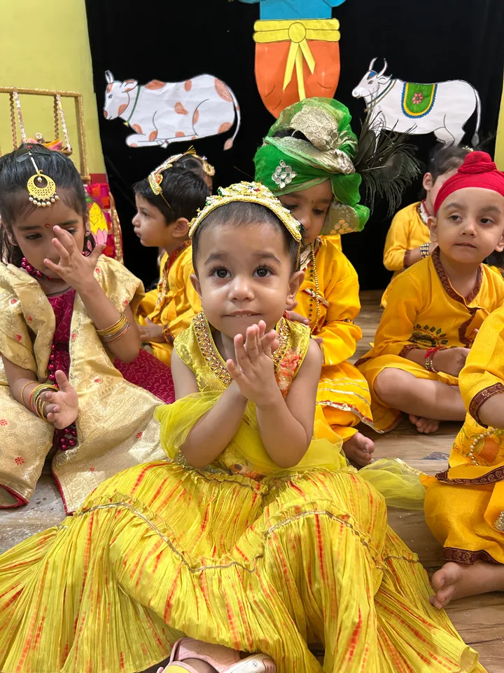 A little girl in a yellow Janmashtami dress clapping her hands