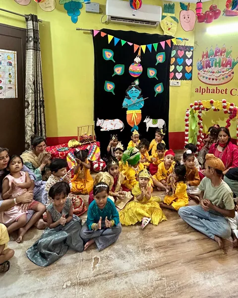 The whole room at Janmashtami: children in yellow sit on the floor beneath a Krishna backdrop and the alphabet CRÈCHE banner, with staff sitting among them