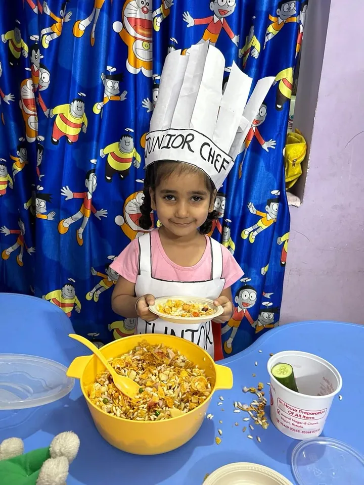 A girl in a Junior Chef hat and apron smiles behind the big yellow mixing bowl