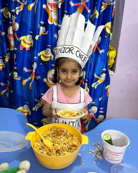 A girl in a Junior Chef hat and apron smiles behind the big yellow mixing bowl