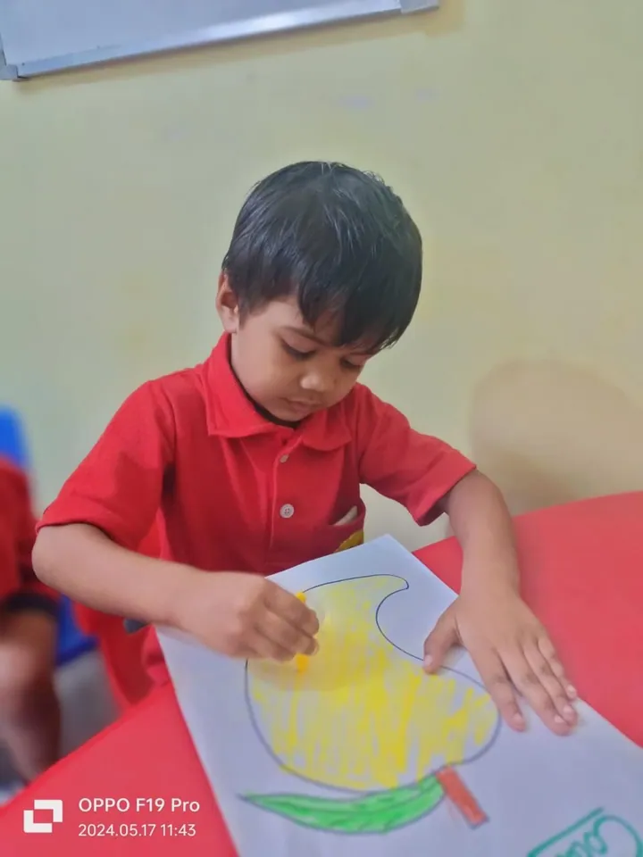 A boy in a red shirt concentrates on colouring his mango yellow