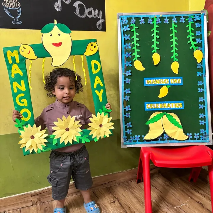A curly-haired toddler stands in the Mango Day frame beside the Mango Day board