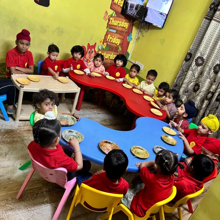 Children in the red uniform sit round the red and blue tables with a plate each