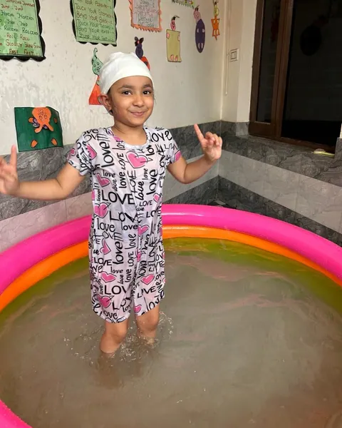 A girl in a patterned swimsuit stands in the paddling pool, pointing up and smiling